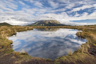 Cloud-covered stratovolcano Mount Taranaki or Mount Egmont reflected in Pouakai Tarn
