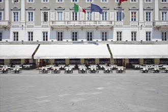 House facade with awnings and empty rows of chairs in front of a cafe on Piazza Unita d' Italia