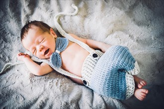 A newborn baby boy sleeping in blue and grey knitted bow tie and trousers