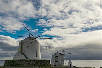 White windmills at the sea in front of cloudy skies