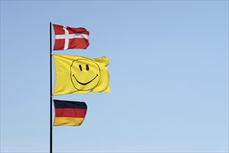 German and Danish flags waving together with a smiley flag on a flagpole