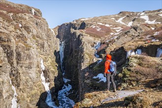 Man in orange jacket standing at the canyon of Glymur Waterfall