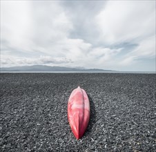 Red inverted canoe on the black stone beach of Albo