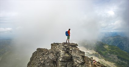 Hiker on the summit of the Hochgolling with rising fog