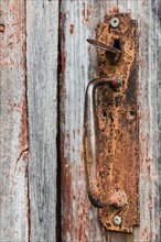 Close-up of rusted metal handle on old wooden grey and red painted barn door
