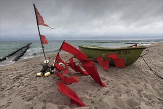 Small fishing boat and buoys with red flags on the beach