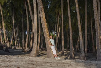 Young beautiful woman leaning on a palm tree in a tropical forest by the beach