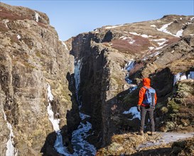 Man in orange jacket standing at the canyon of Glymur Waterfall