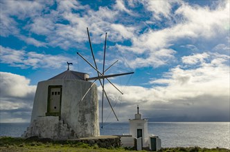 White windmill at the sea in front of a cloudy sky