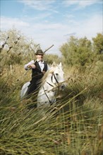 Gardian or traditional bull herder in typical working clothes galloping on a Camargue horse