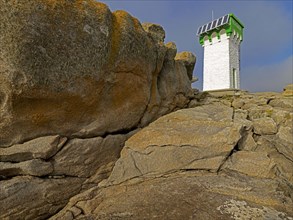 Green and white lighthouse on granite rocks