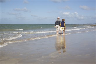 Elderly couple walks barefoot through the water on the beach