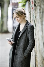 Young woman leans against a wall and looks at her smartphone