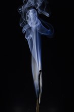 Burned match with blue smoke in front of a dark background