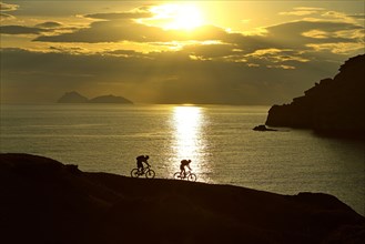 Two mountain bikers cycling on a rocky coast