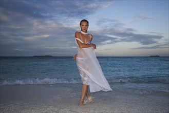 Young woman posing in wet white cloth on the beach at dusk