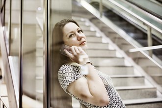 Young woman posing with smartphone behind a glass wall in an underground station