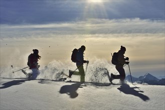 Three snowshoe walkers run in the snow against the light