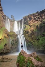 Young woman standing on a stone in front of Ouzoud waterfalls and cascades