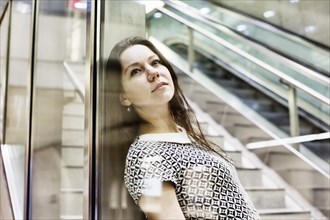 Young woman posing behind a glass wall in an underground station