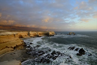 Rocky coast with arch La Portada at sunset with clouds