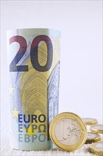 Rolled upright twenty Euros bank note with one Euro coin