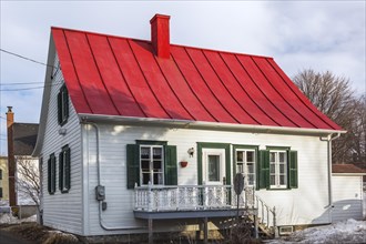 Rear of old 1835 white wood plank with green trim Canadiana cottage style house with red sheet metal roof in early spring