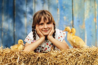 Nine year old girl lying with three ducklings in the straw