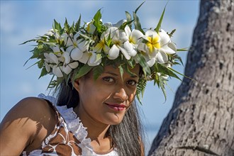 Young woman with flower wreath from Frangipani leaning on palm trunk