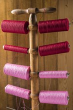 Thread stand in front of wooden wall with cotton thread reels