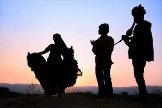 Woman dancing in front of the setting sun with two musicians