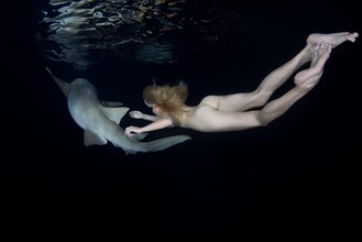 Nude beautiful woman swimming at night with a shark