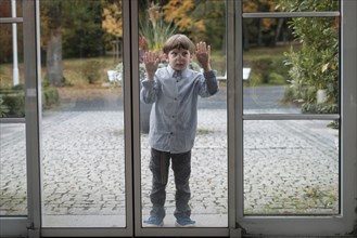 Child squeezes nose and hands on glass panel