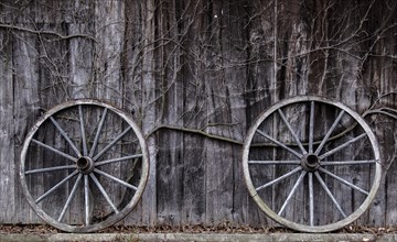 Two wagon wheels leaning against a barn wall