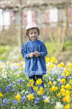 Little girl standing in a flowery meadow of daffodils
