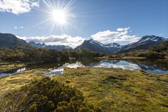 Sun shining on small mountain lake with reflection of a mountain chain