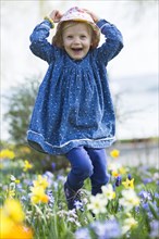 Little girl running through a flowery meadow of daffodils