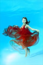 Young woman with red dress posing under water