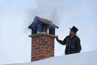 Chimney sweeper in winter on a roof with smoky chimney