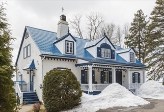Old 1920s white roughcast with blue trim cottage style home facade with blue steel tile roof in early spring