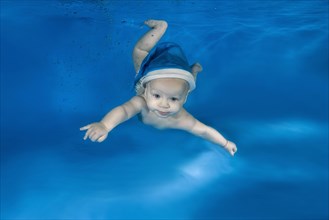 Baby boy in Santa's blue cap swims underwater in a pool