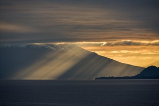 Sun rays shine through dark cloudy sky in front of Osorno Volcano at Llanquihue Lake