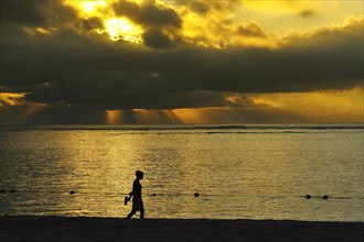 Woman walking at sunset with cloudy atmosphere on the beach Le Morne