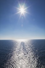 Ship's wake and sunburst over shimmering Mediterranean sea in late afternoon off the coast of Italy