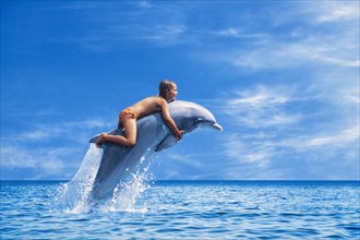 Six year old girl riding a dolphin leaping out of the sea