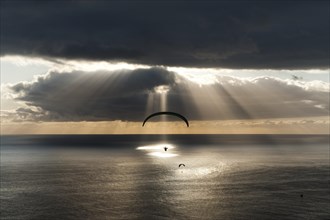 Sun shines behind dark clouds with paraglider over the Atlantic