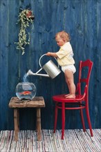 Three year-old girl pouring water in a goldfish bowl