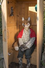 Straw doll fox sitting in outhouse