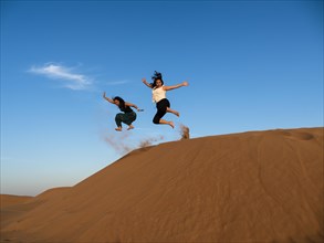 Two young women jumping from sand dune in desert