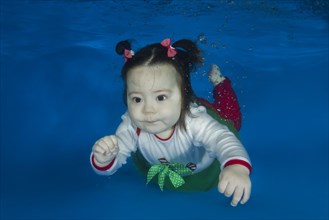Little girl in a beautiful bright dress swimming under water in a pool